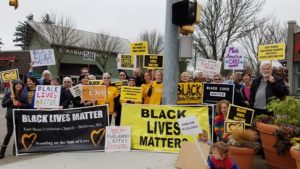 More than 20 people of all ages stand on a street corner in Woodinvill, Washington behind signs and banners supporting Black Lives