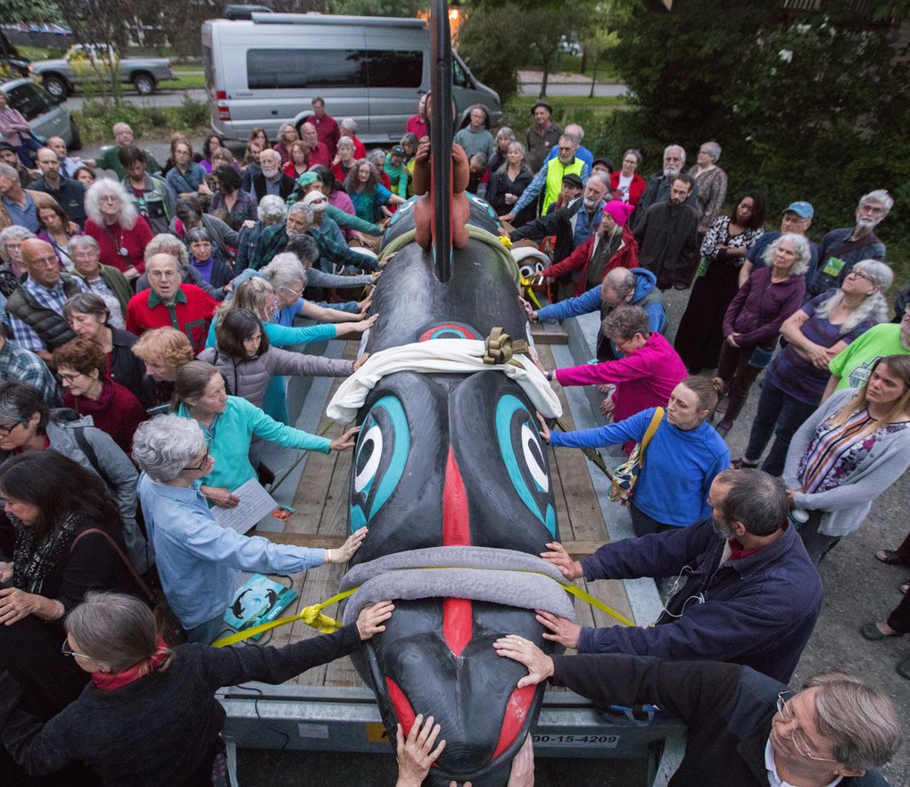 People placing hands on totem pole for blessing